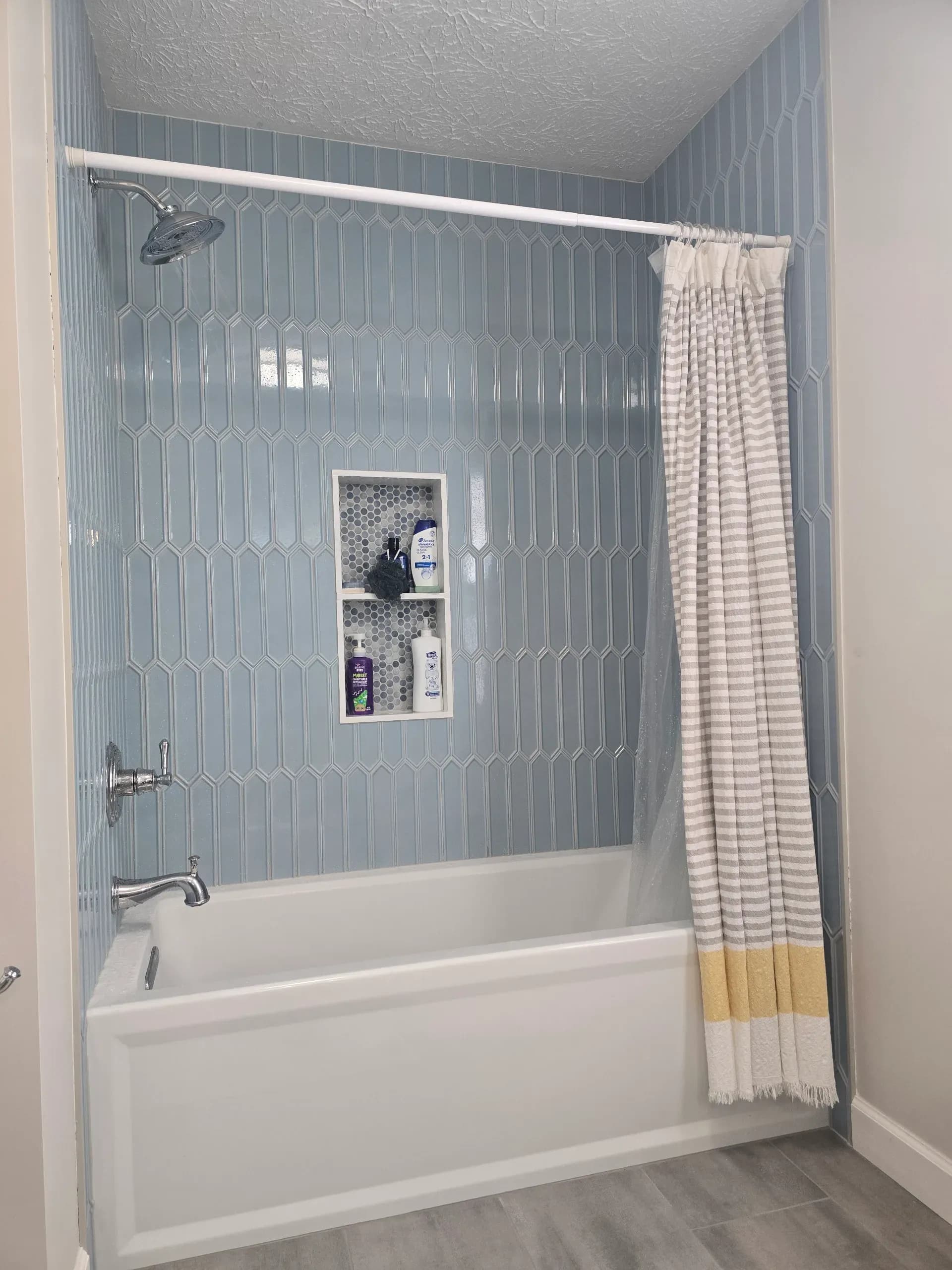 Blue geometric-tile shower with white tub, niche shelves, chrome fixtures, and striped curtain in Alpharetta bathroom