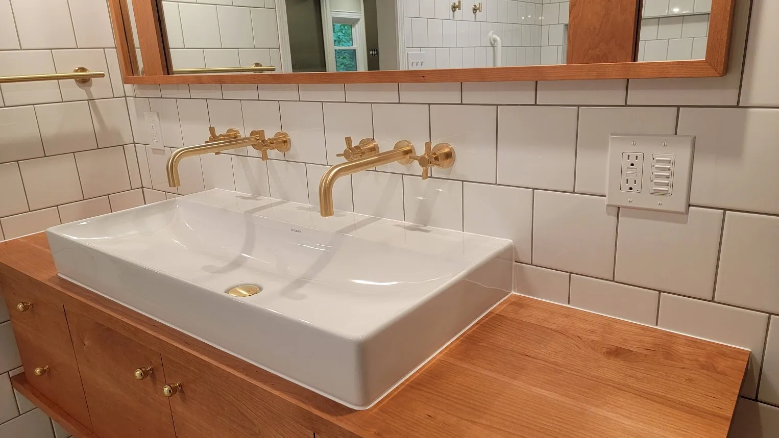Bathroom vanity with white subway tile backsplash, brass wall faucets, wood counter, and mirror