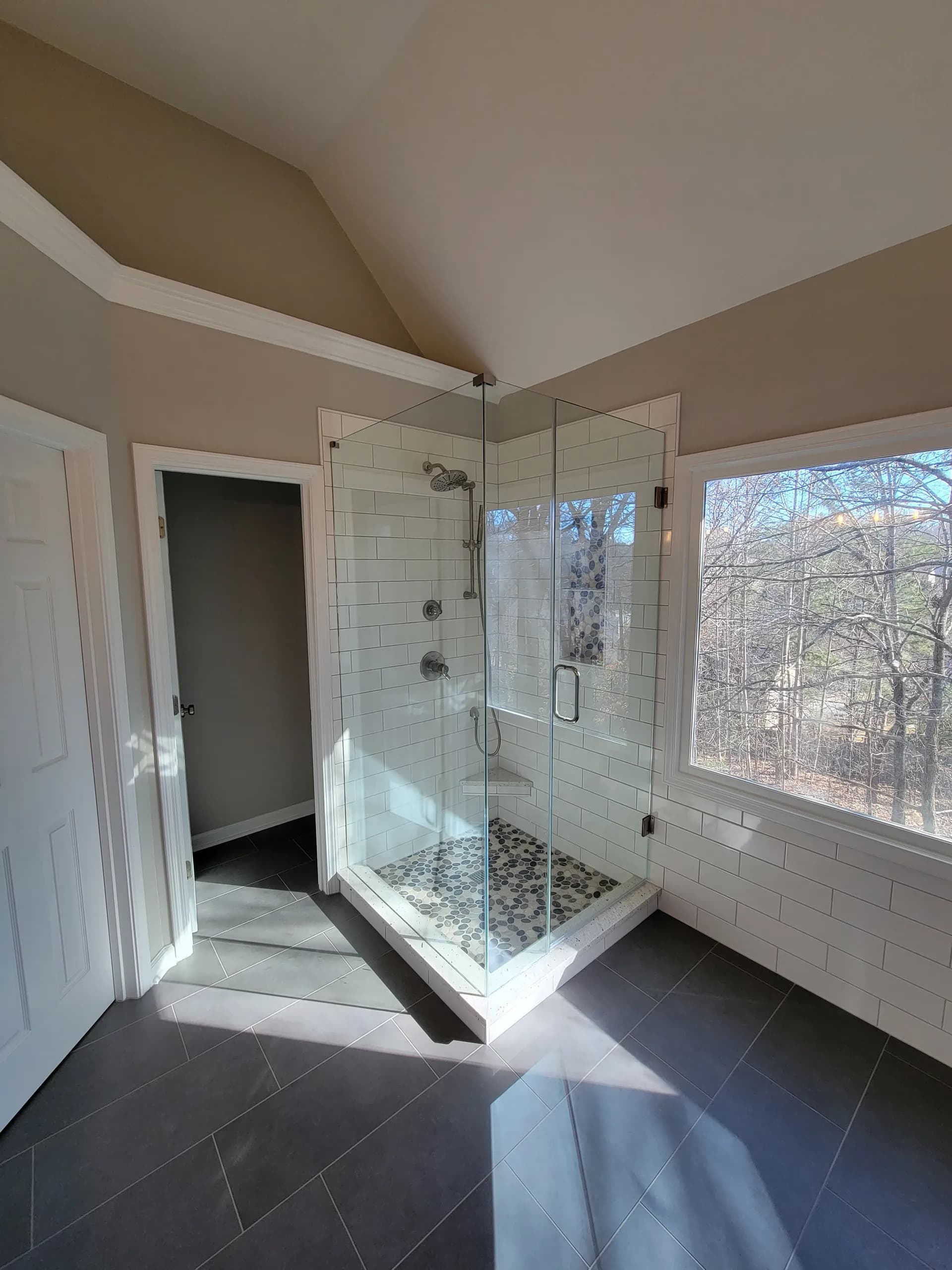 Modern bathroom with glass corner shower, white subway tile, dark floor tile, and large window view