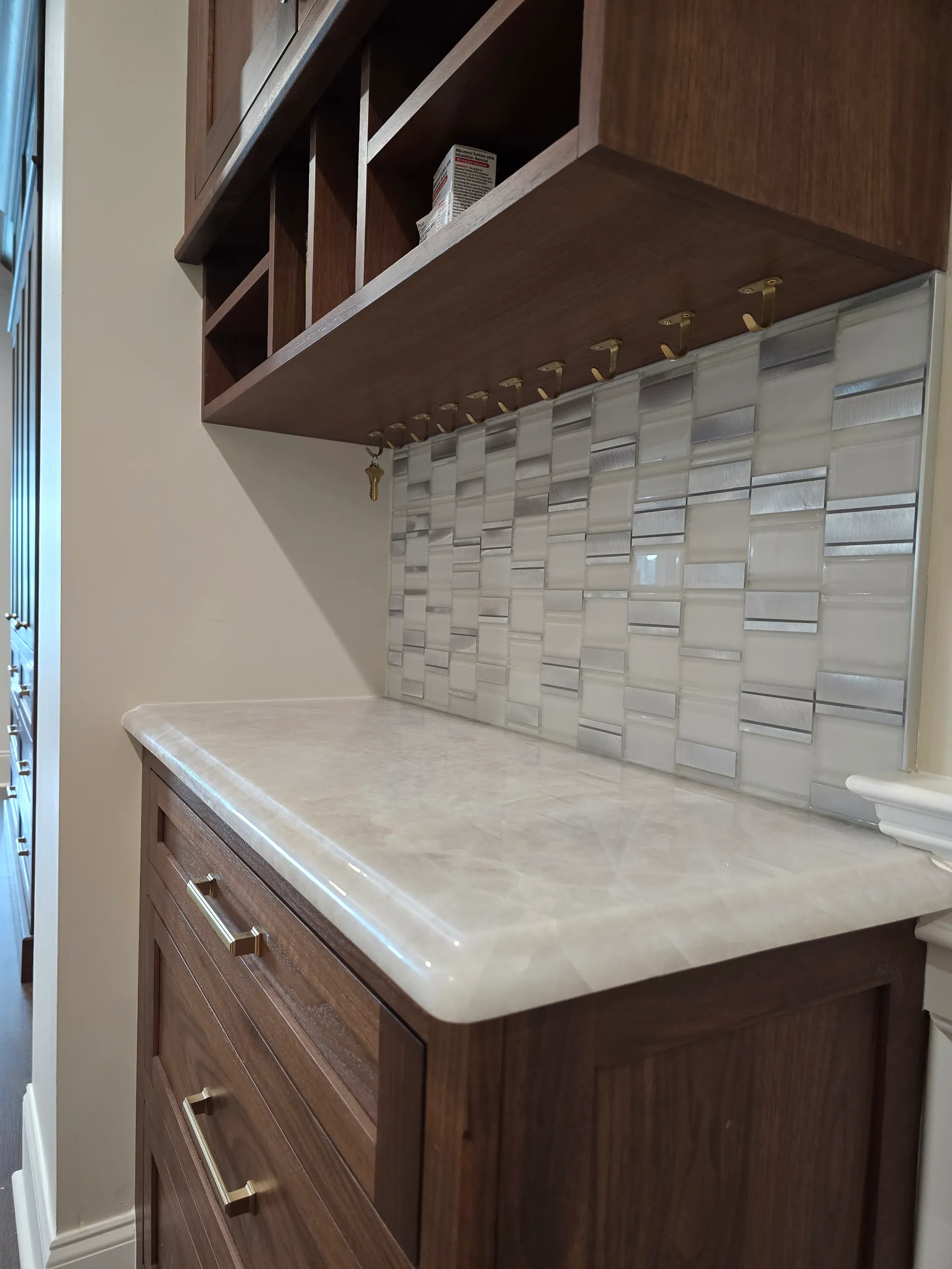 Kitchen backsplash with white and gray glass mosaic tiles above a countertop and wooden cabinets with spice rack hooks