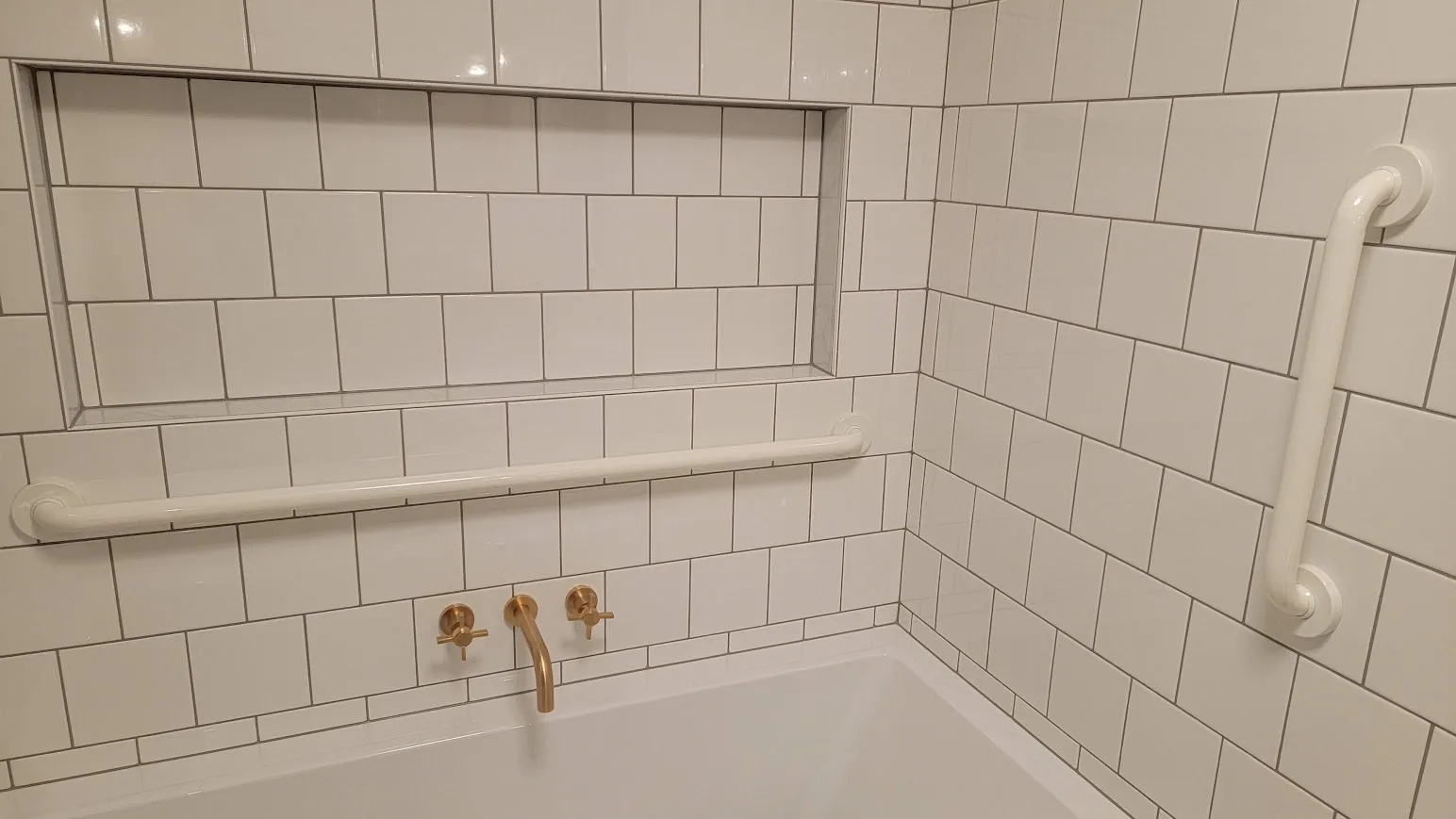 White subway-tile shower with brass faucet, niche, and grab bars in a clean bathroom