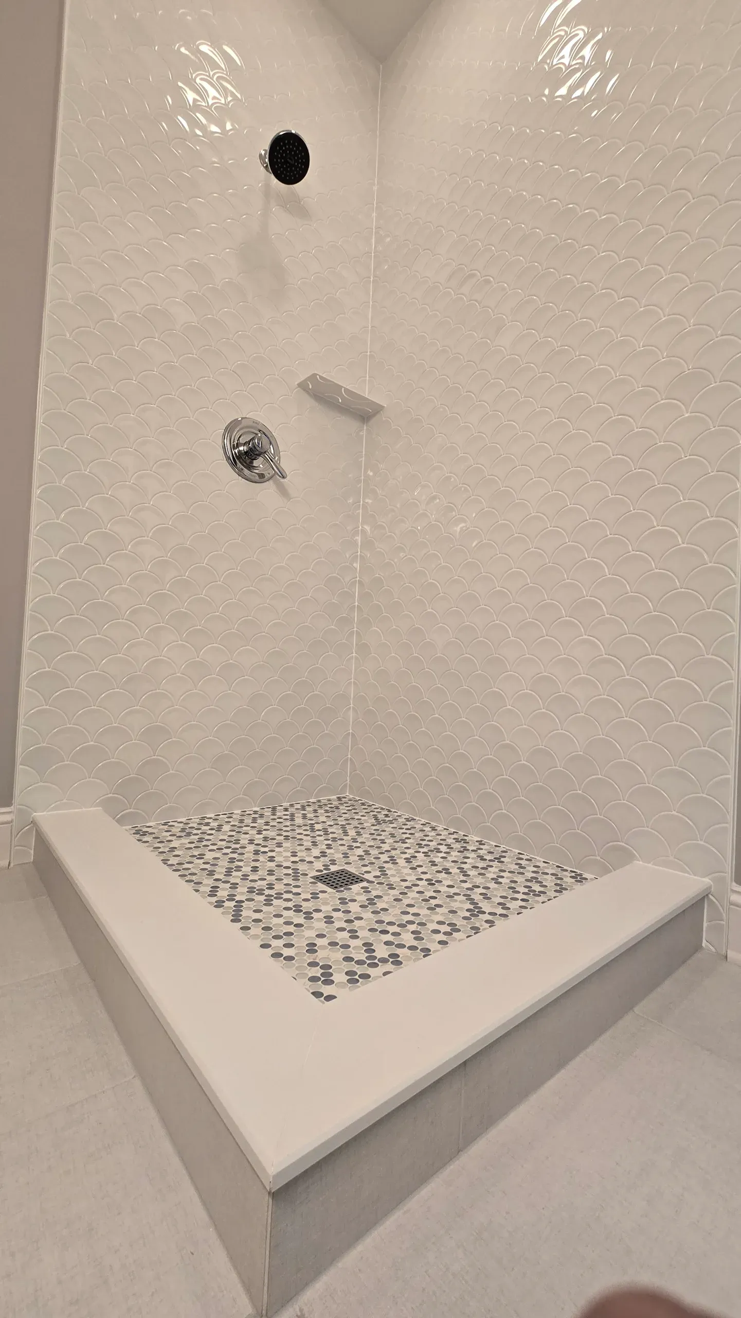 White tiled shower with scallop wall tiles, mosaic shower floor, and chrome shower fixtures in a modern bathroom