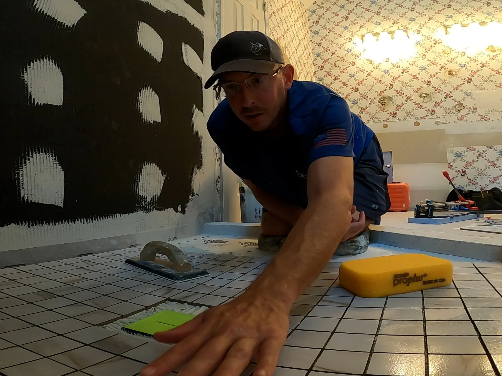 Tile installer spreading adhesive on a bathroom floor with a trowel, preparing for tile installation.