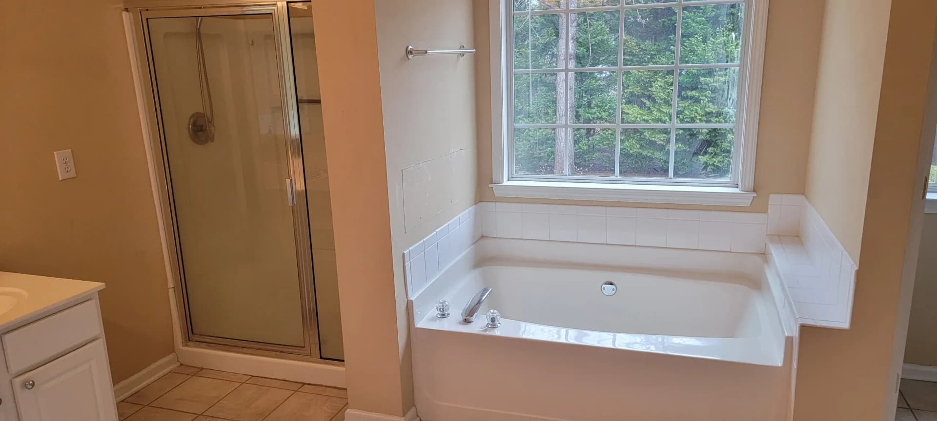 Bathroom with white tub surround tile, glass shower, window, and beige walls in Marietta, GA