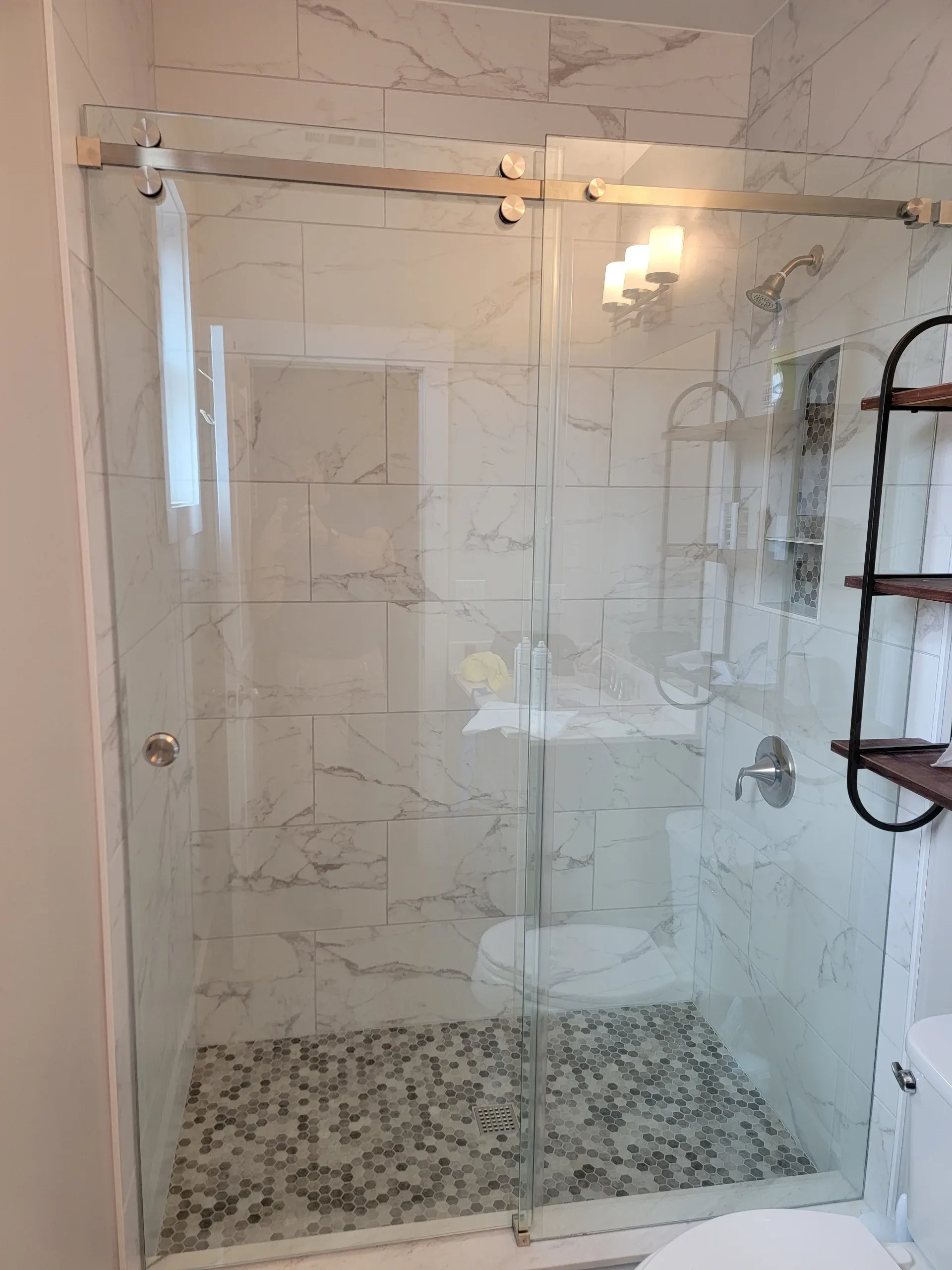 Frameless glass shower with marble-look wall tile and hex mosaic floor in a bright bathroom