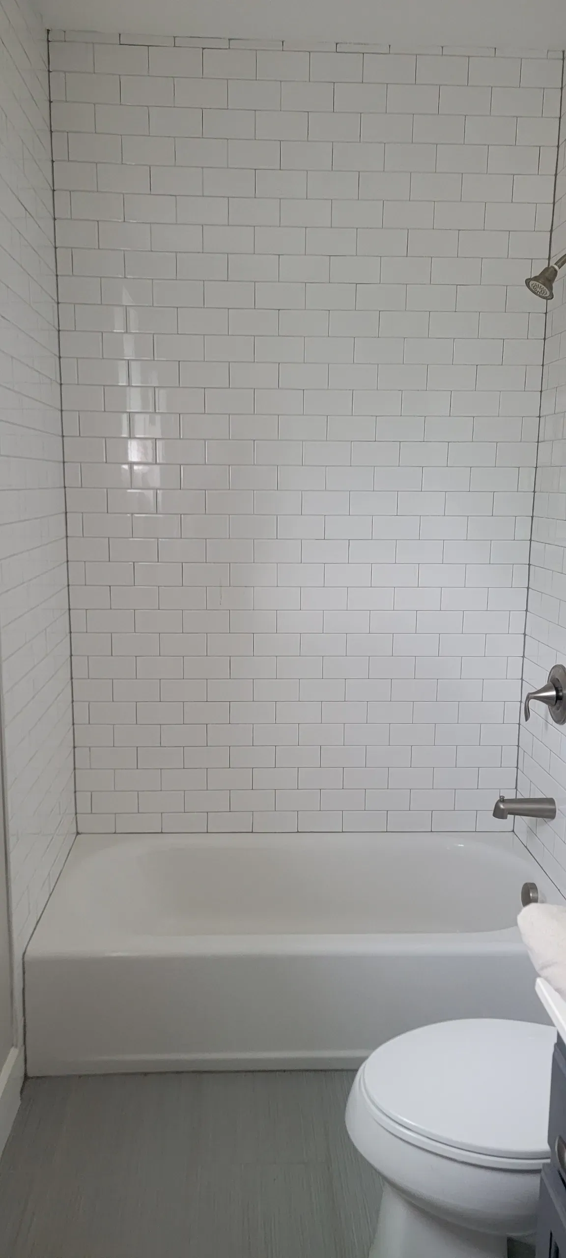 White subway-tile shower alcove with bathtub, gray floor, and toilet visible in a bathroom corner