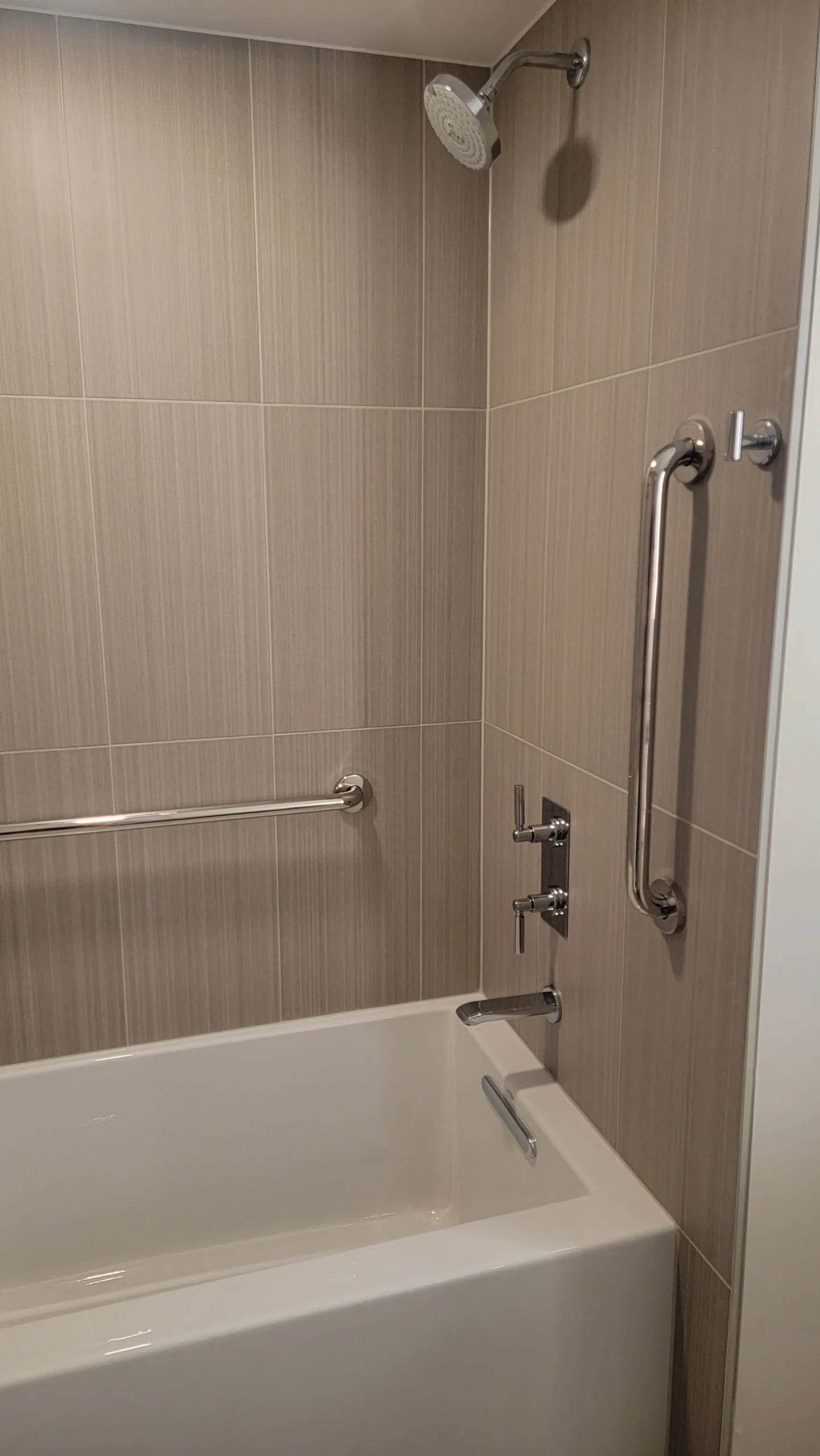 Tiled bathtub shower with beige wall tiles, chrome grab bars, and showerhead in a bathroom