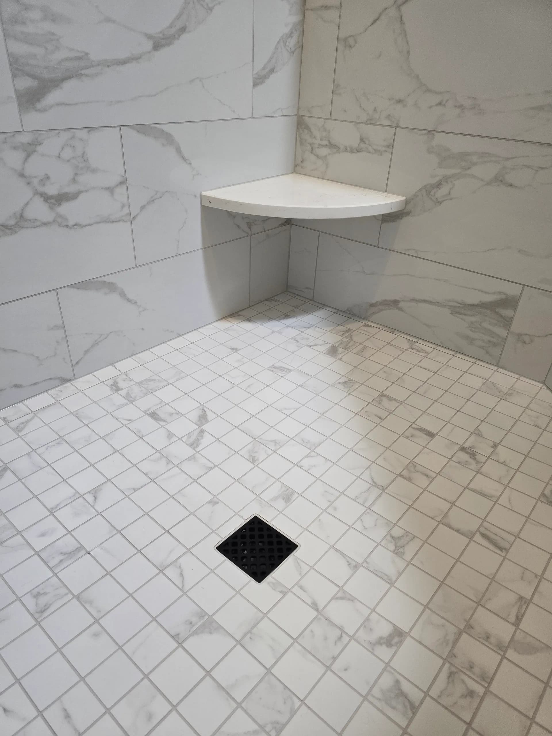 Marble-look tiled shower with corner shelf and square floor drain in a clean, modern bathroom finish